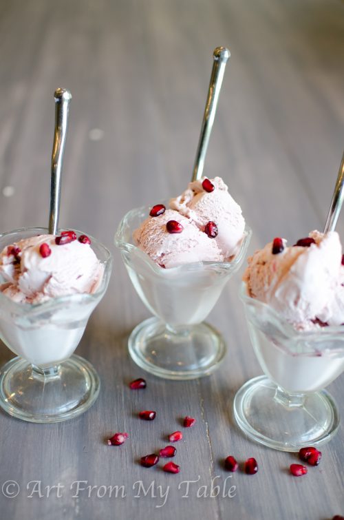 Three dishes of pomegranate ice cream with spoons and pomegranate arils. 