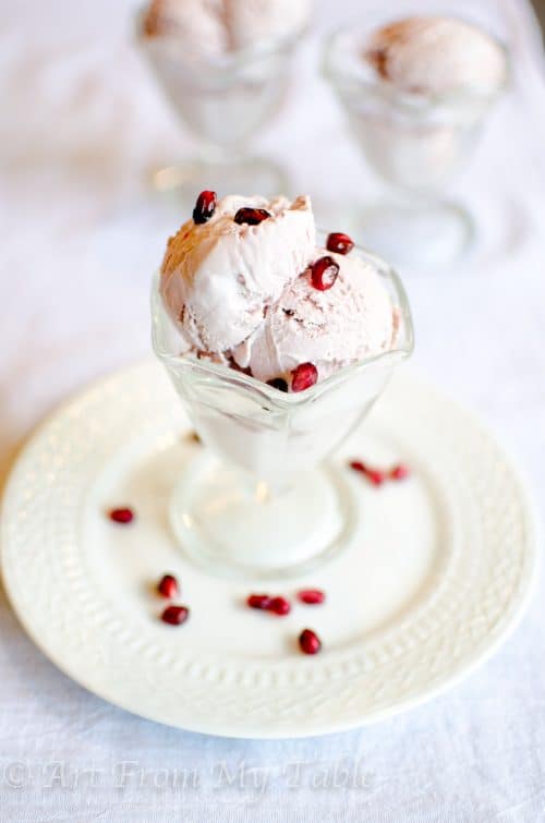 Pomegranate ice cream in a dessert dish with pomegranate arils (seeds) on it. 