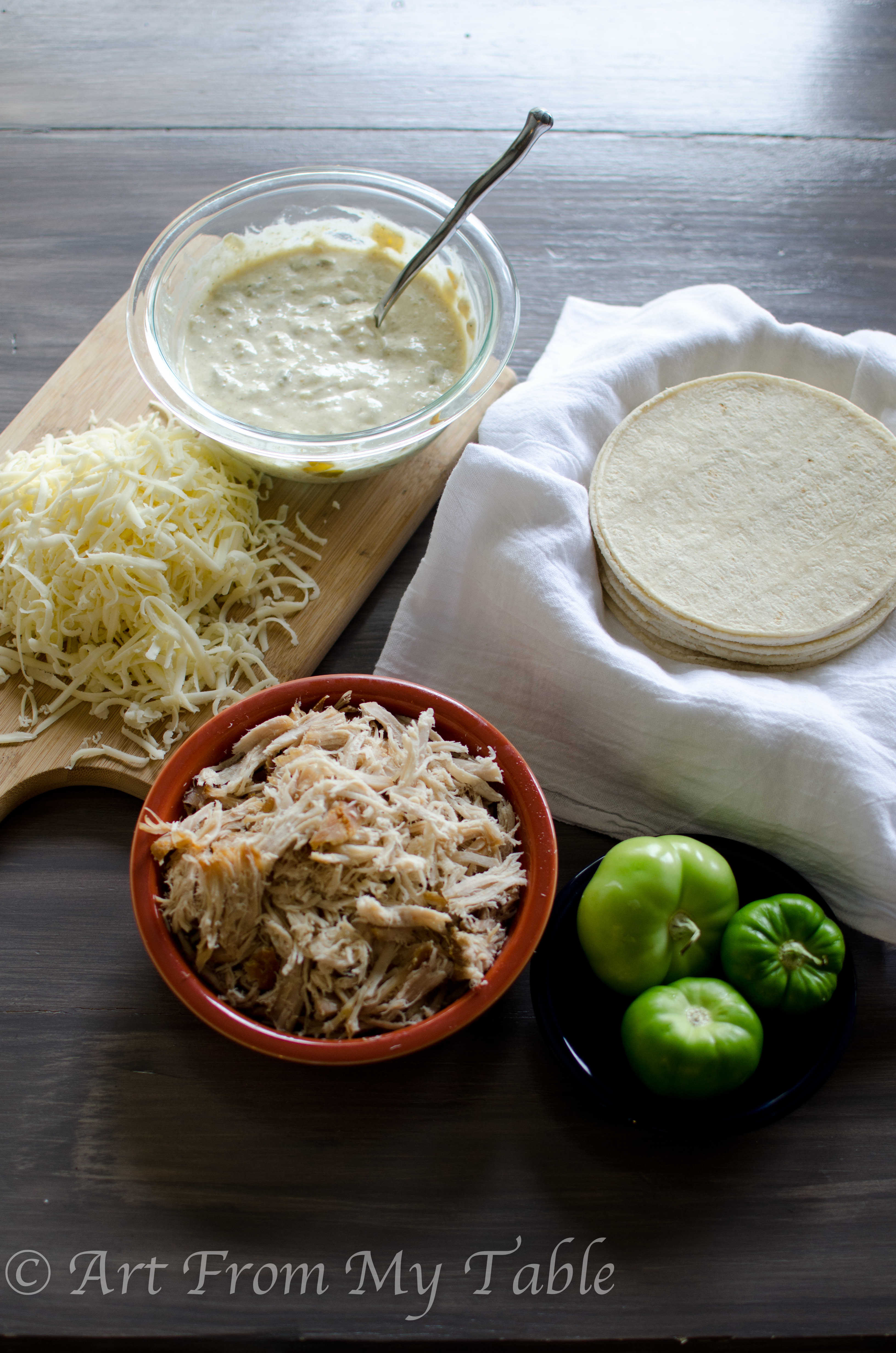 Prepped ingredients for carnitas casserole verde, shredded cheese, green salsa sauce, shredded pork, corn tortillas.