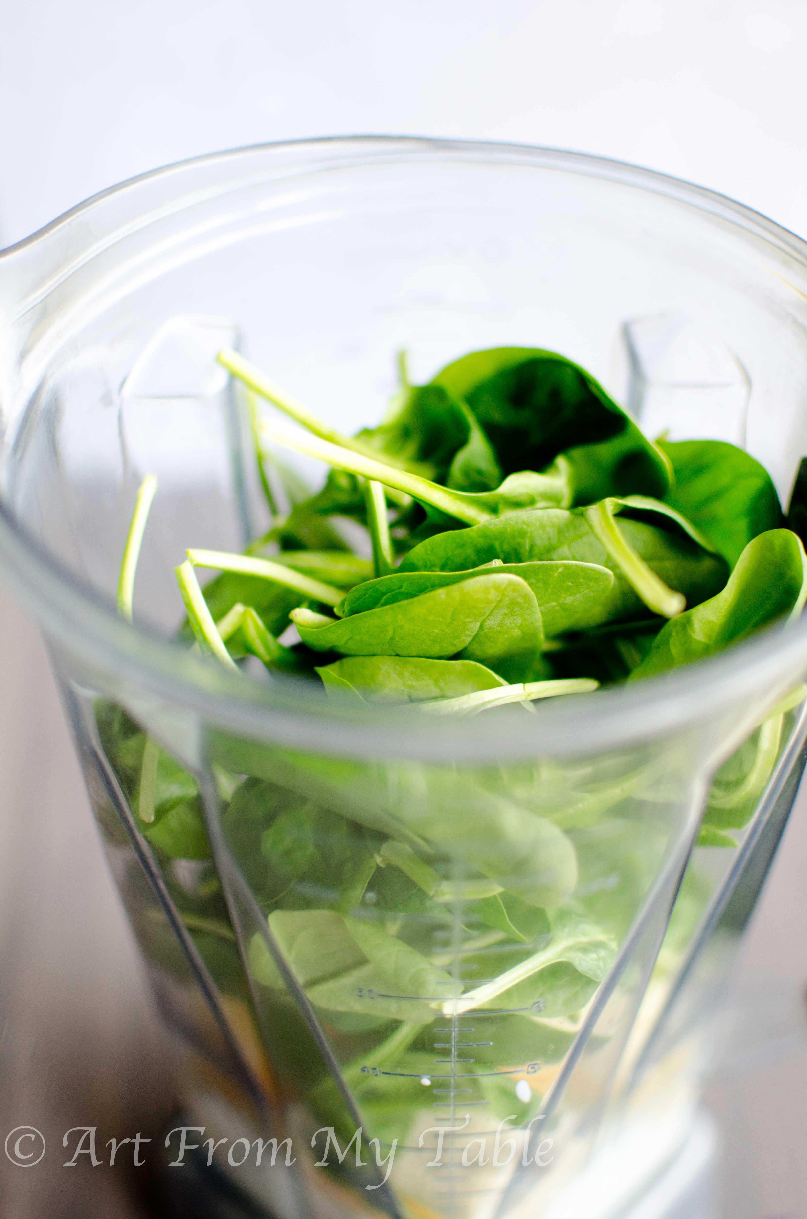 blender full of spinach leaves, banana, yogurt and other smoothie ingredients.