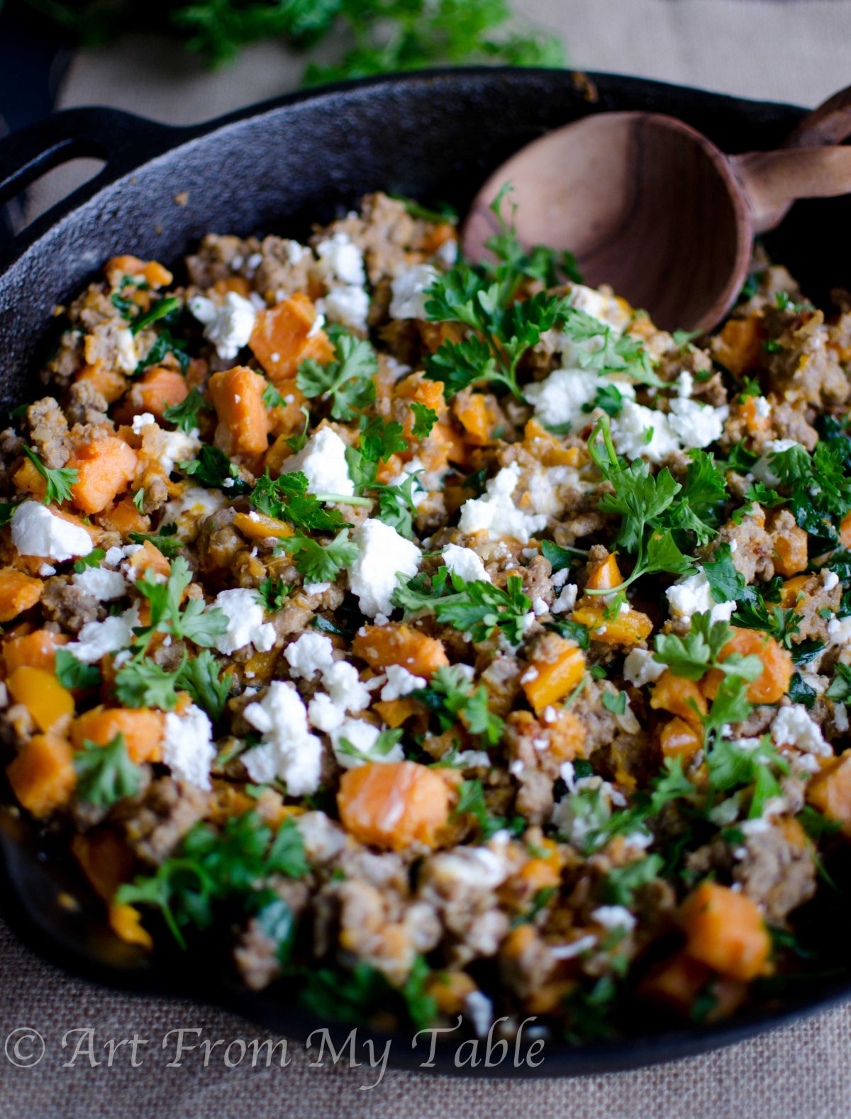 Turkey skillet dinner is a cast iron skillet full of ground turkey, kale, sweet potato chunks and goat cheese garnished with fresh parsley