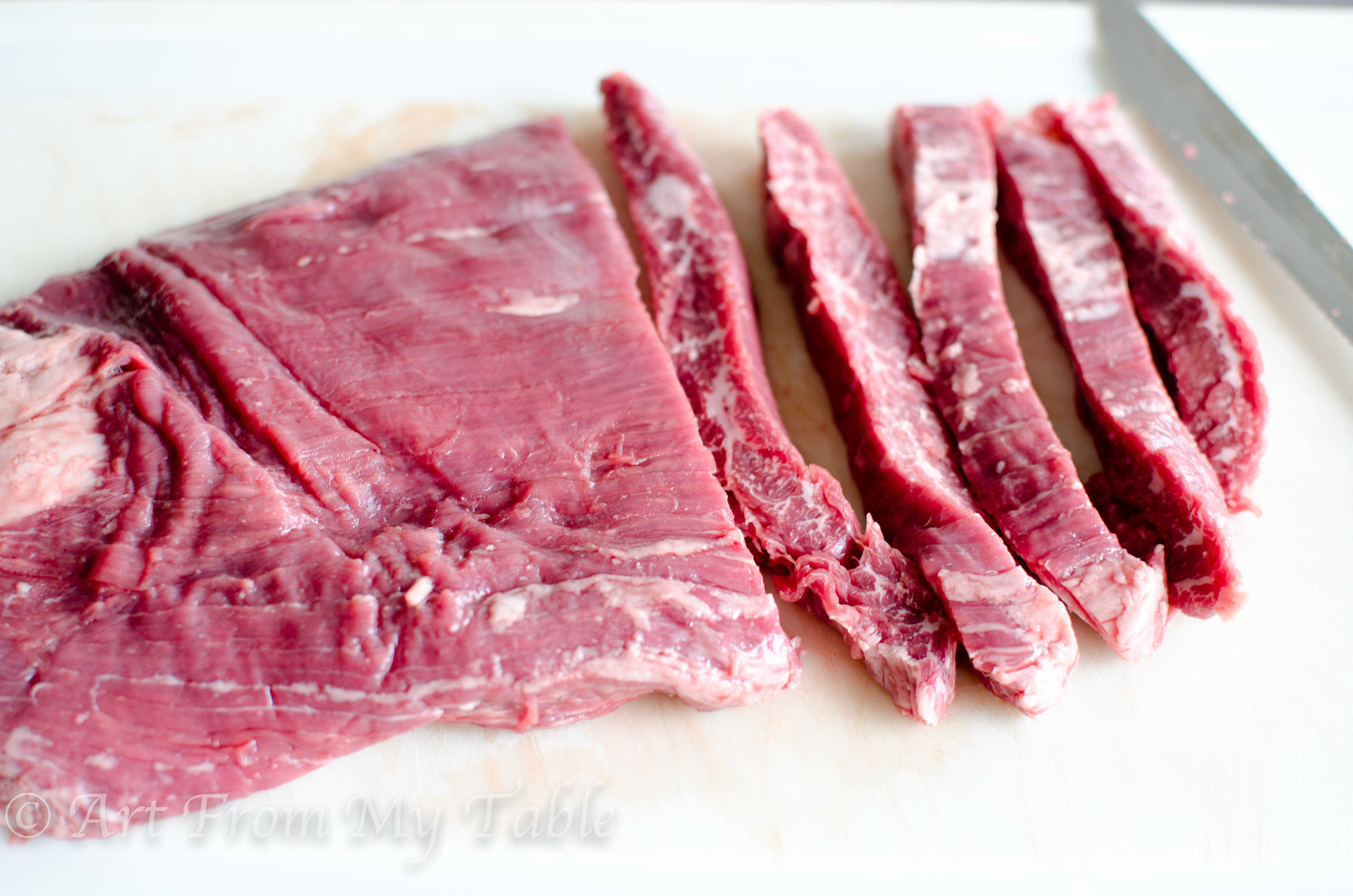 Raw flank steak, partially sliced into 1/2 inch slices. 