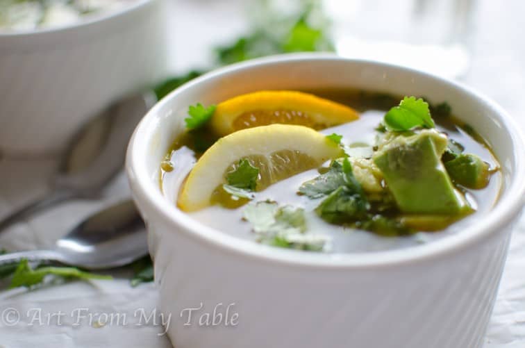 Bowl citrus chicken soup garnished with orange slice and avocado and cilantro.