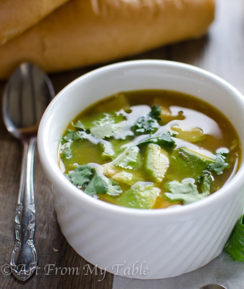 Bowl of citrus chicken soup garnished with cilantro, served with bread.