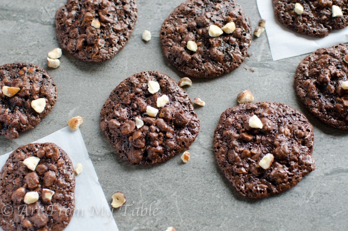 chocolate hazelnut drop cookies on a counter sprinkled with chopped hazelnuts. 