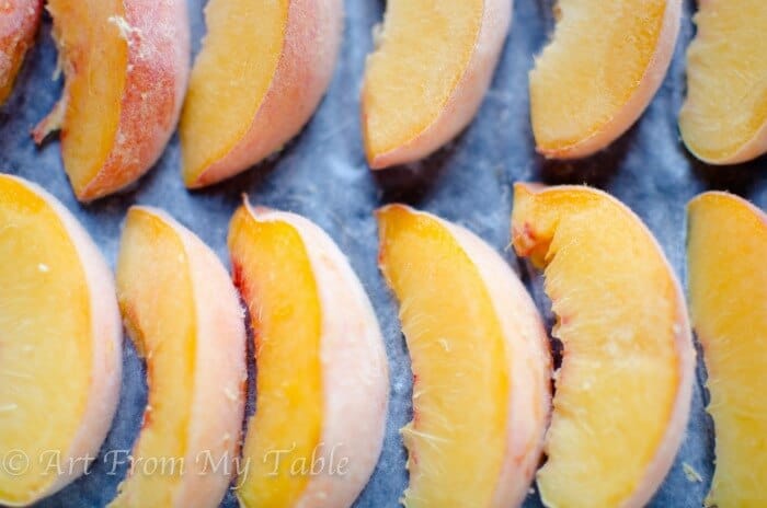 Peach slices after flash freezing without sugar, on a rimmed baking sheet. 