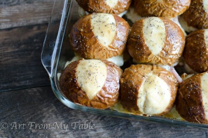 Baked ham and cheese sliders on soft pretzel  buns in a casserole dish after baking. 