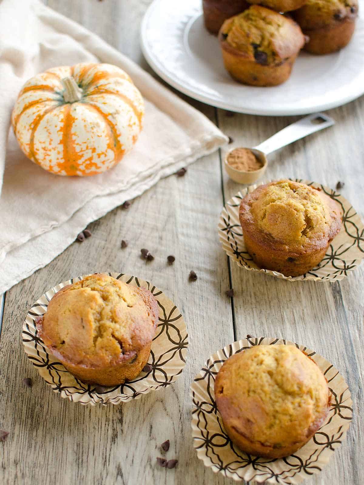 3 pumpkin chocolate chip muffins with wrappers peeled away, garnished with chocolate chips