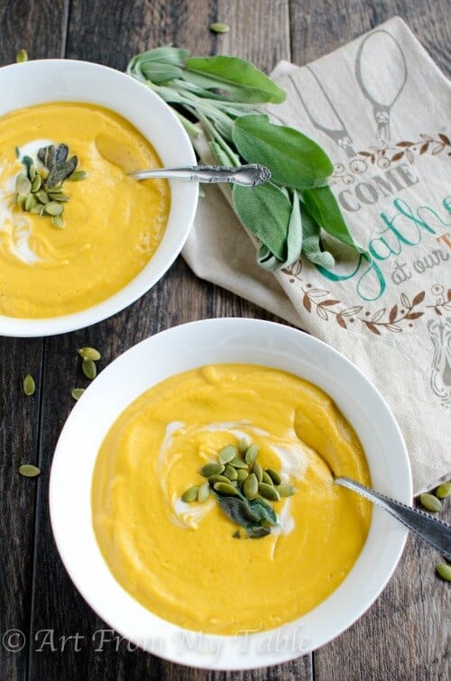 Two bowls of smoky pumpkin soup garnished with pepitos and fresh sage.