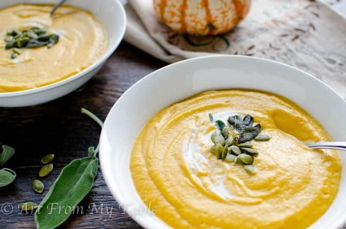 Bowl of smoky pumpkin soup with pepitas and a spoon dipping in it.