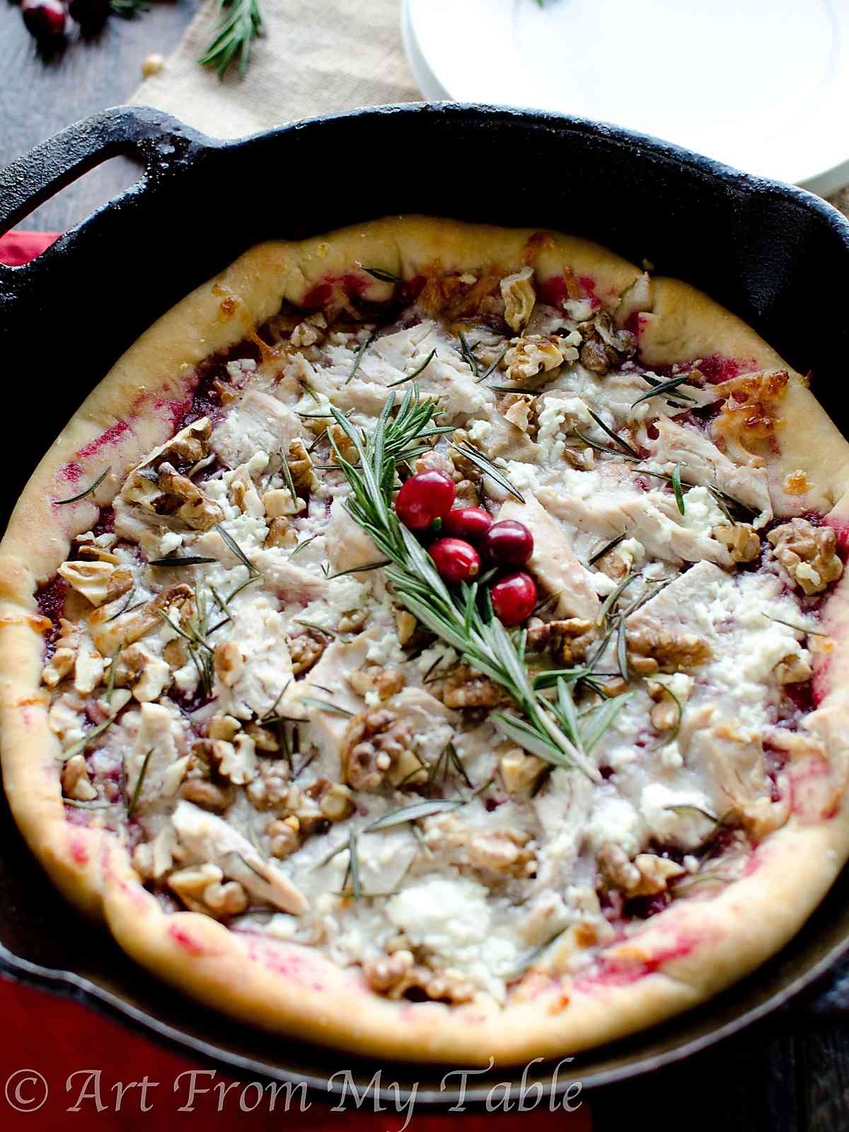 Pizza in a cast iron pan with turkey, cranberry sauce, walnuts, cheese and fresh rosemary.