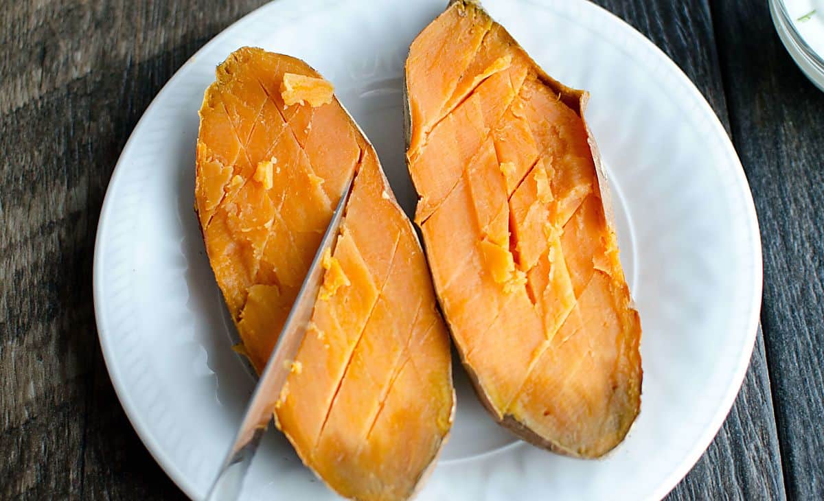 baked sweet potato sliced in half with a knife making diagonal cuts.