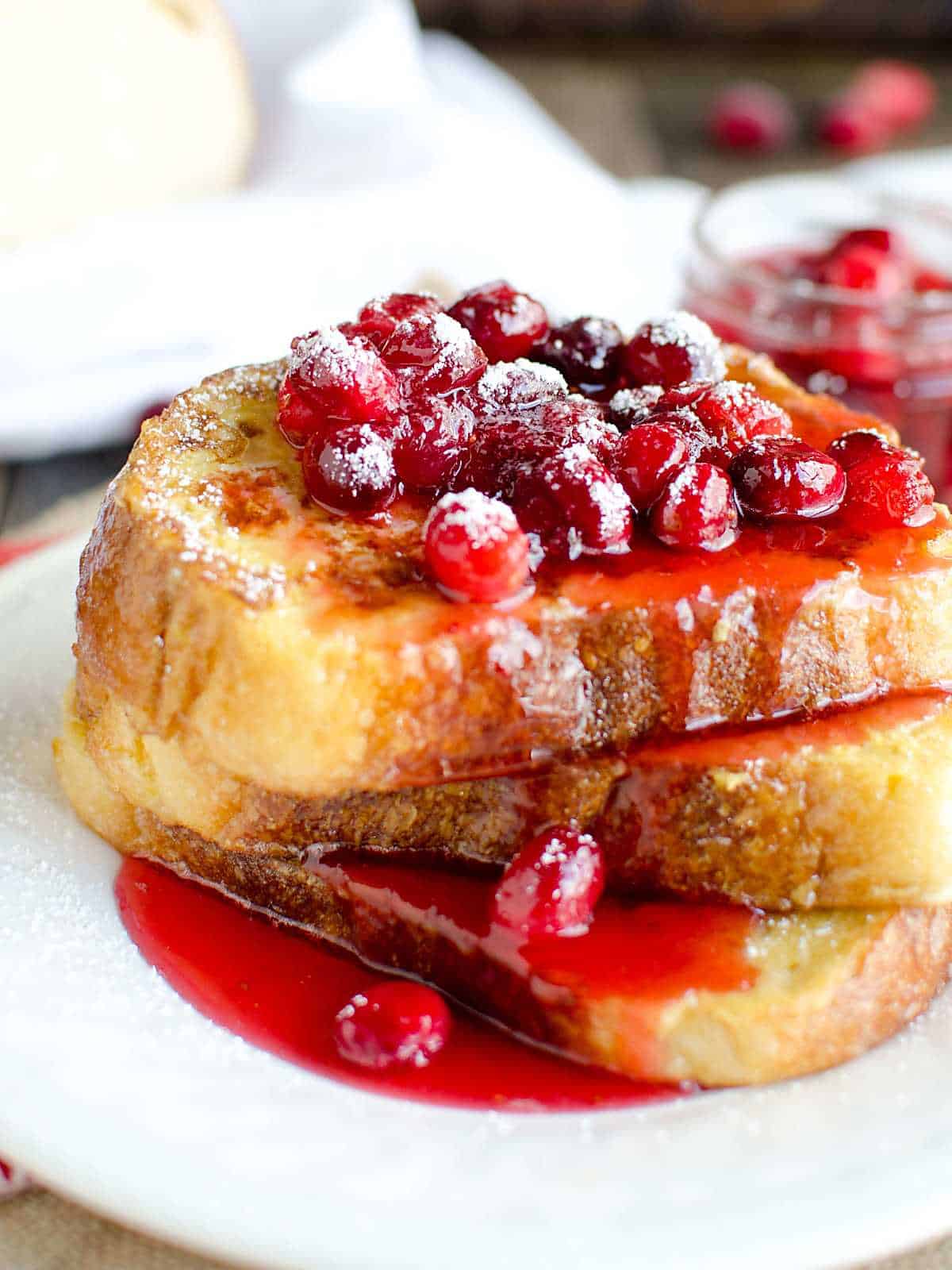 eggnog french toast stacked on a white plate topped with cranberry syrup and powdered sugar.