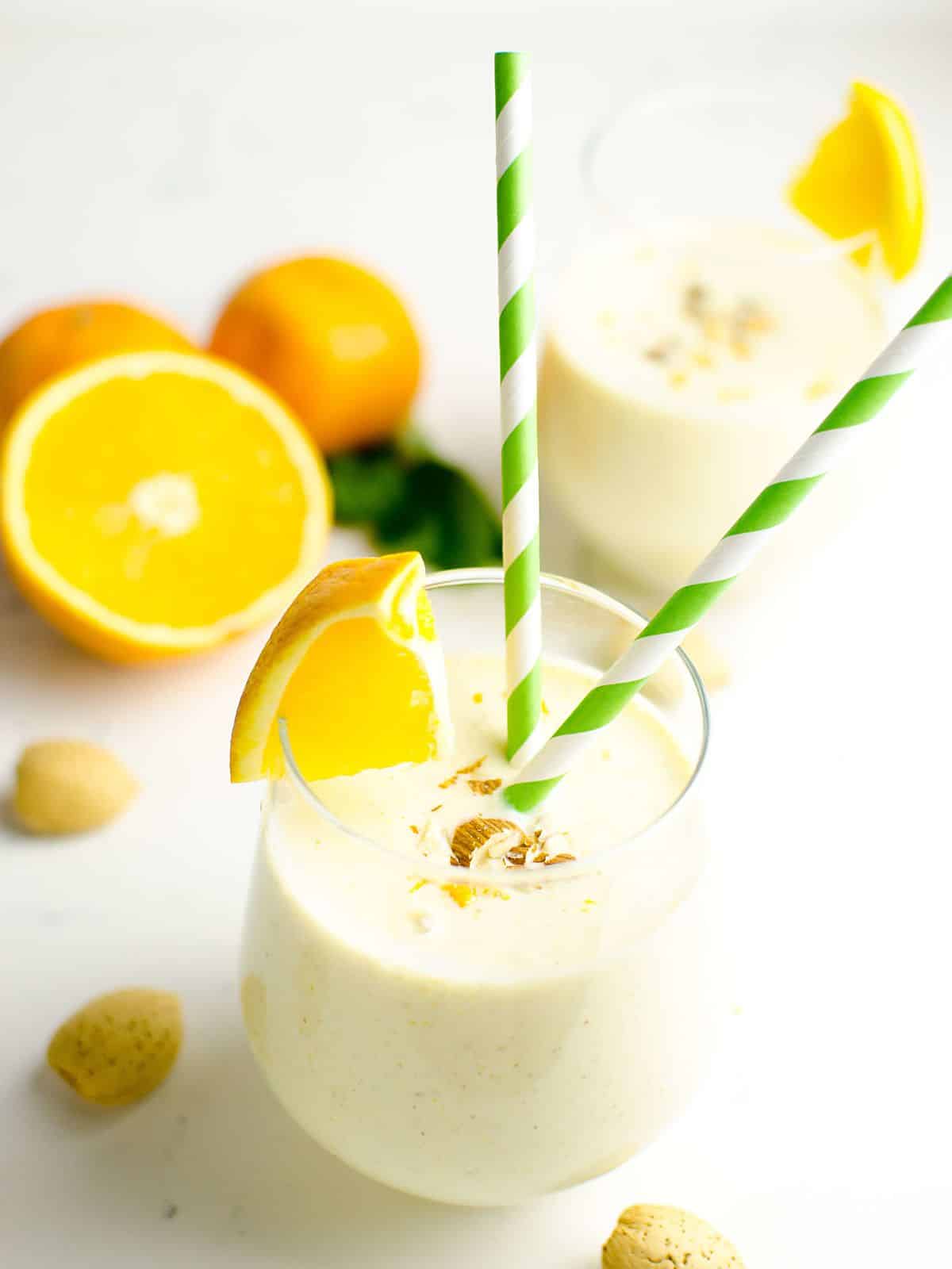 Two Orange Vanilla Smoothies in glasses garnished with chopped almonds and an orange wedge.