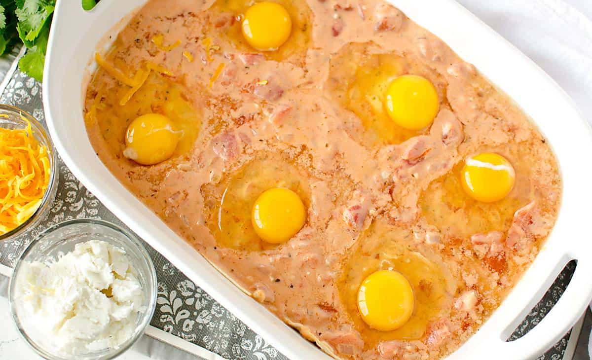 tomato cream sauce in a casserole dish with raw eggs and whole yolks on top, ready to be baked.