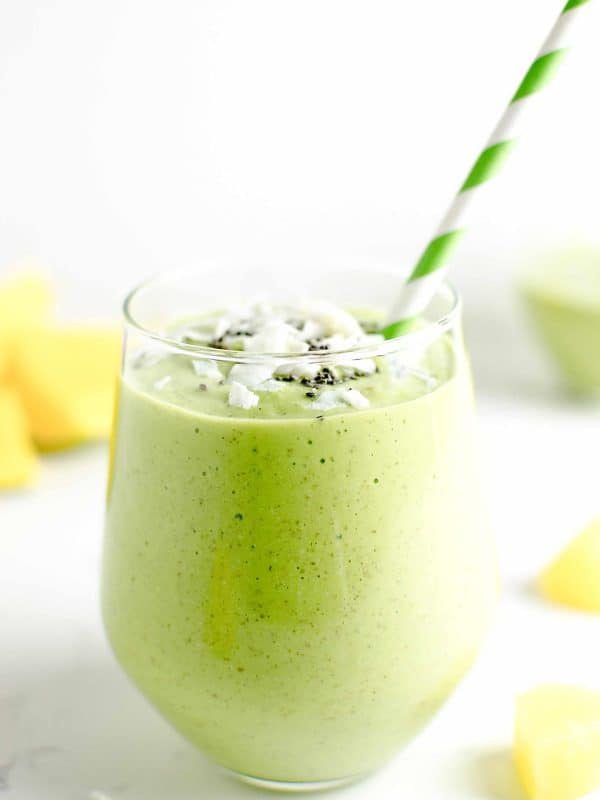 tropical green smoothie in a glass garnished with coconut chips and chia seeds.