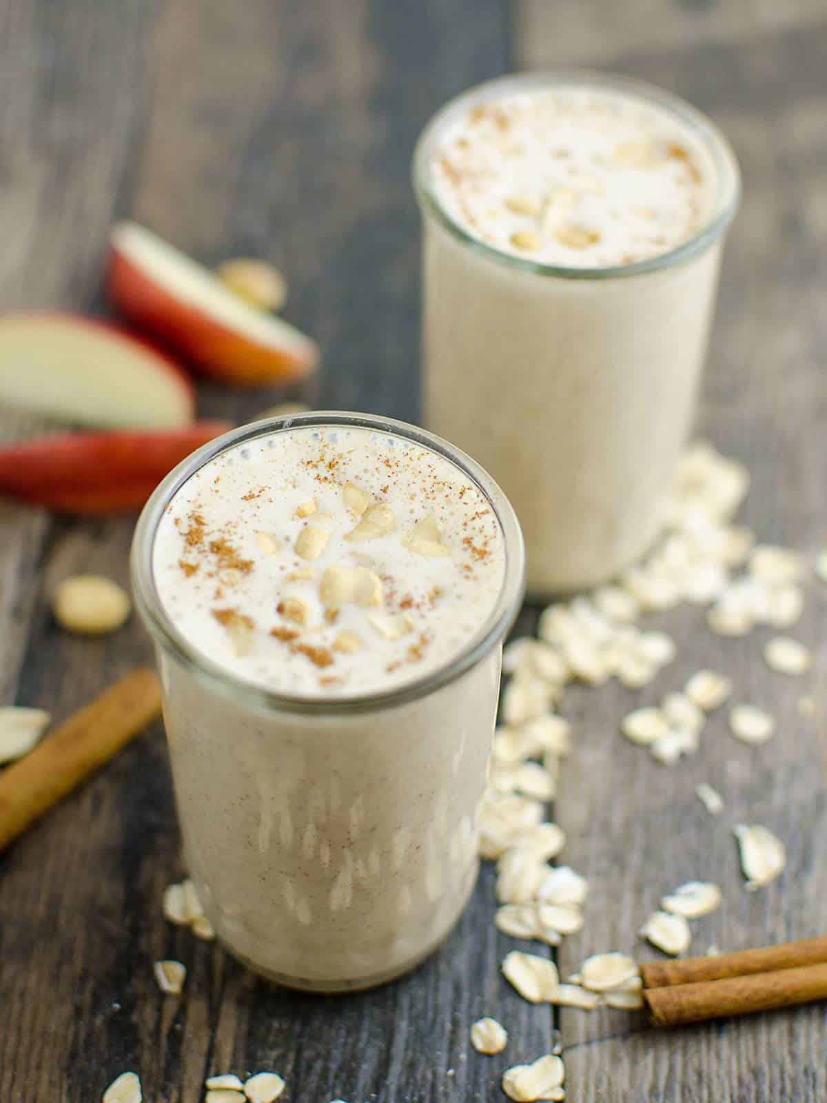 Two healthy apple pie smoothies in glasses garnished with ground cinnamon and chopped peanuts.