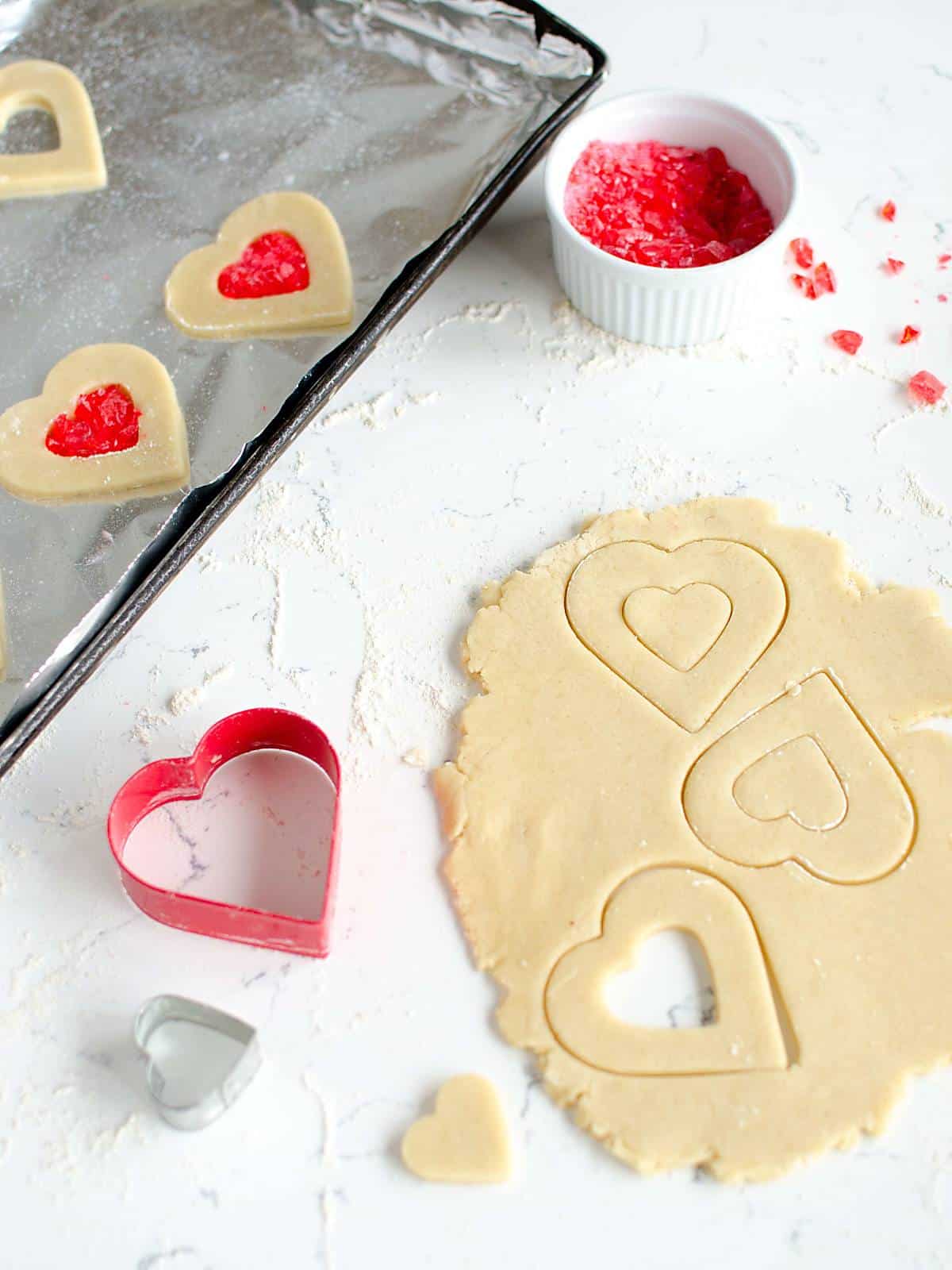 rolled cookie dough with heart shaped cookie cut outs, cookie cutters, and crushed red candy