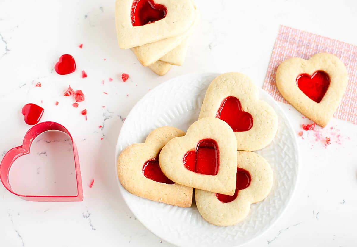 Valentine De-Coder Cookies, plate of heart shaped cookies with a red hard candy center, coded message and cookie cutter.