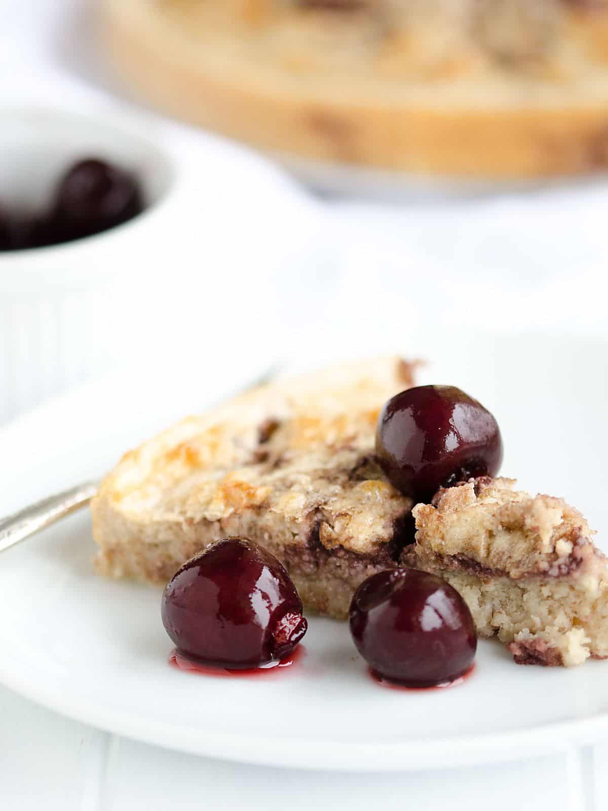 Slice of Black Cherry Breakfast Cake on a white plate with juicy black cherries.