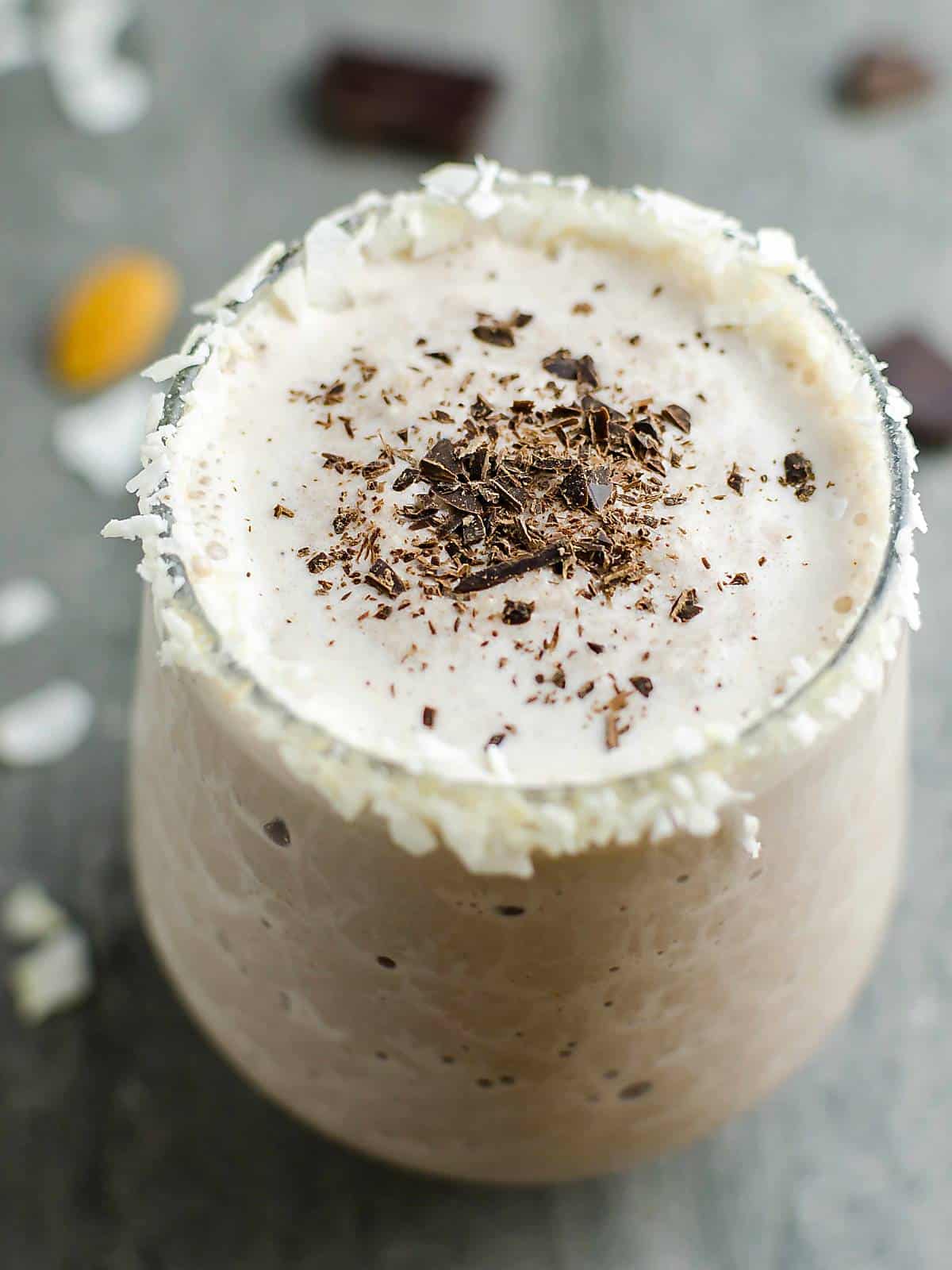 healthy almond joy smoothie in a glass rimmed with shredded coconut. Smoothie is topped with shaved dark chocolate.