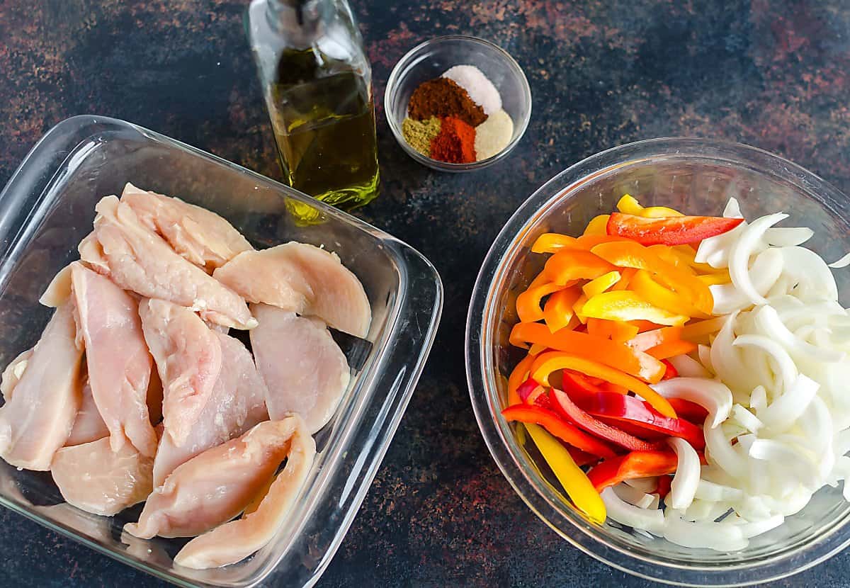 ingredients for sheet pan chicken fajitas: chicken tenders, sliced bell peppers and onions, olive oil and spice mixture including chili powder, cumin, garlic,, salt, paprika.