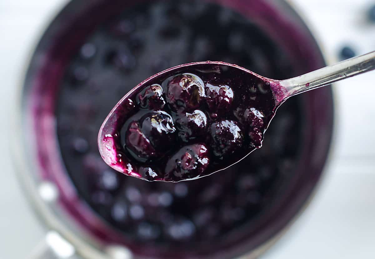spoonful of fresh blueberries that have been cooked over the pan of cooked berries.