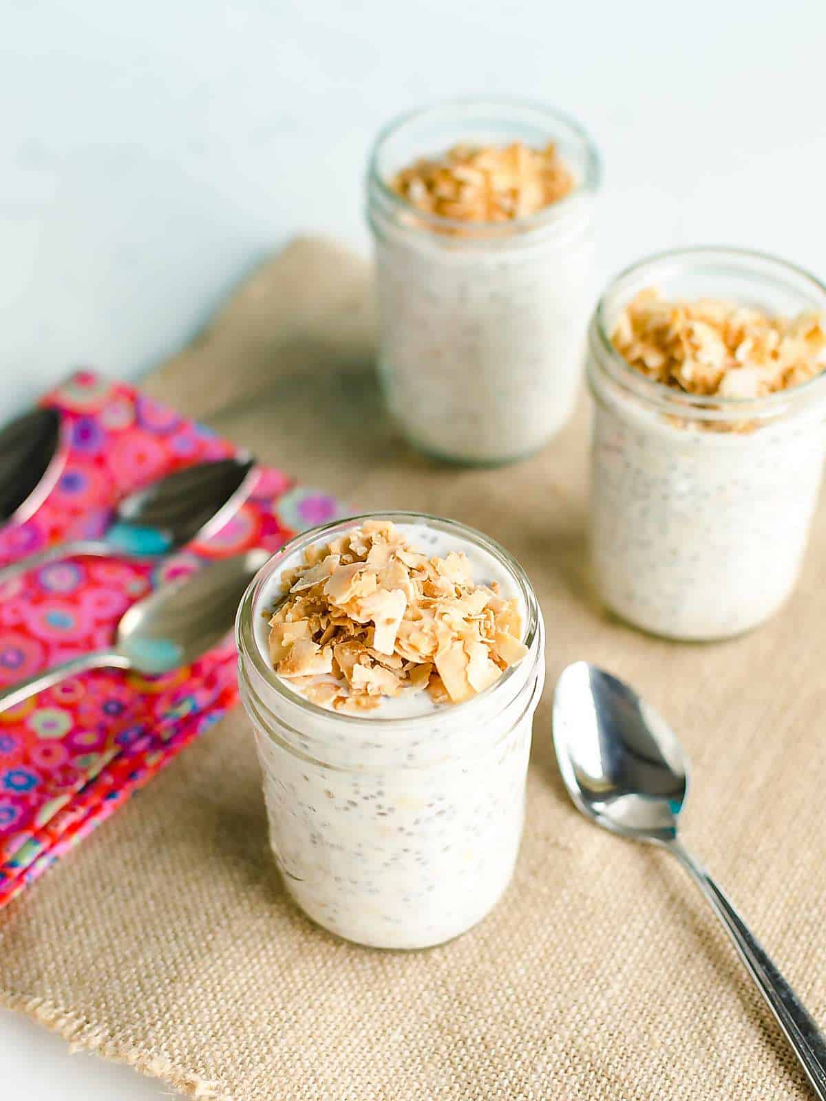 three glasses of prepared overnight oats topped with toasted coconut.
