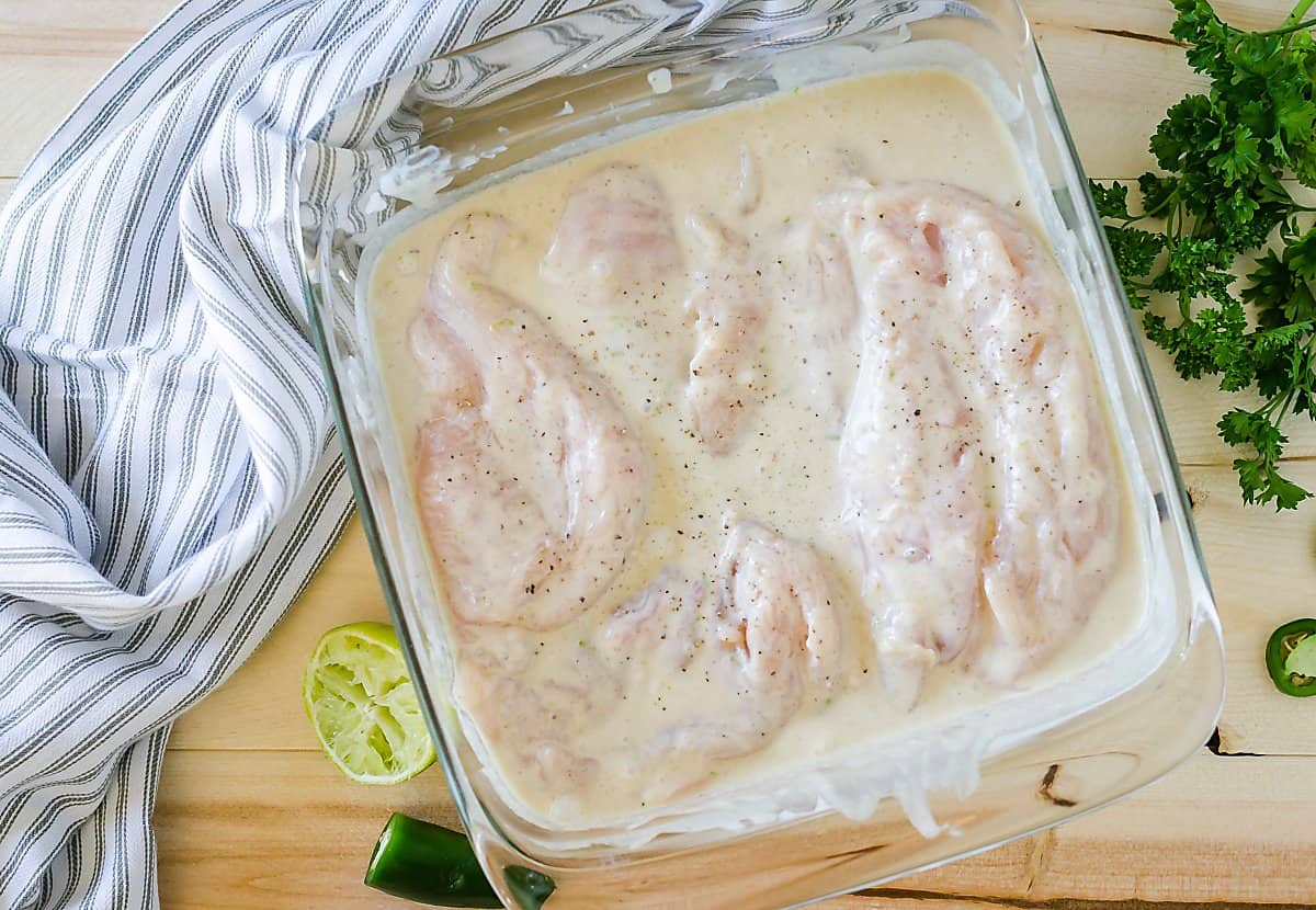 raw chicken breasts in coconut lime marinade in an 8x8 glass dish.