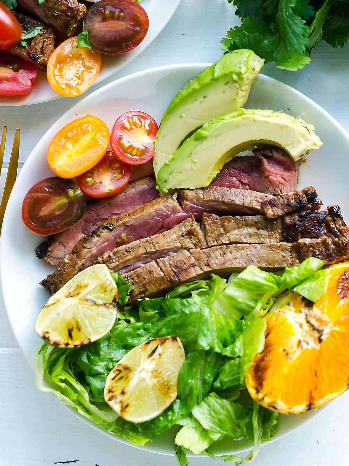 carne asada grilled to medium rare on a plate with lettuce, tomatoes and avocados.
