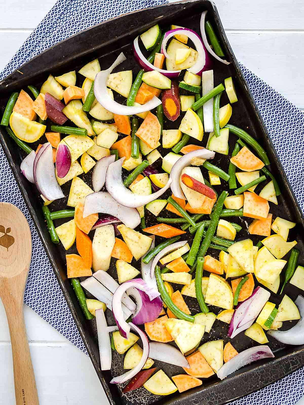 sheet pan full of cut up raw colorful vegetables with a wooden spoon on the side
