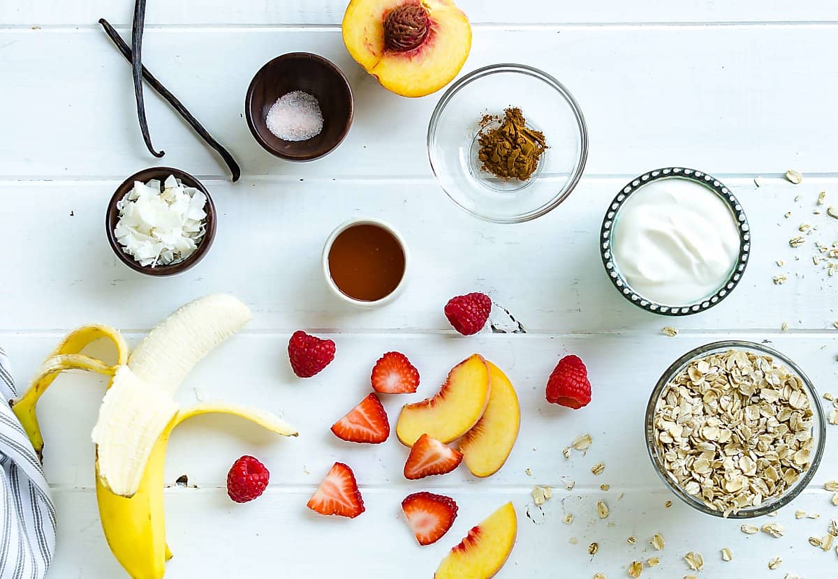 ingredients for breakfast granola cups: banana, coconut flakes, vanilla bean, salt, cinnamon, honey, yogurt, rolled oats, sliced strawberries, sliced peaches, raspberries