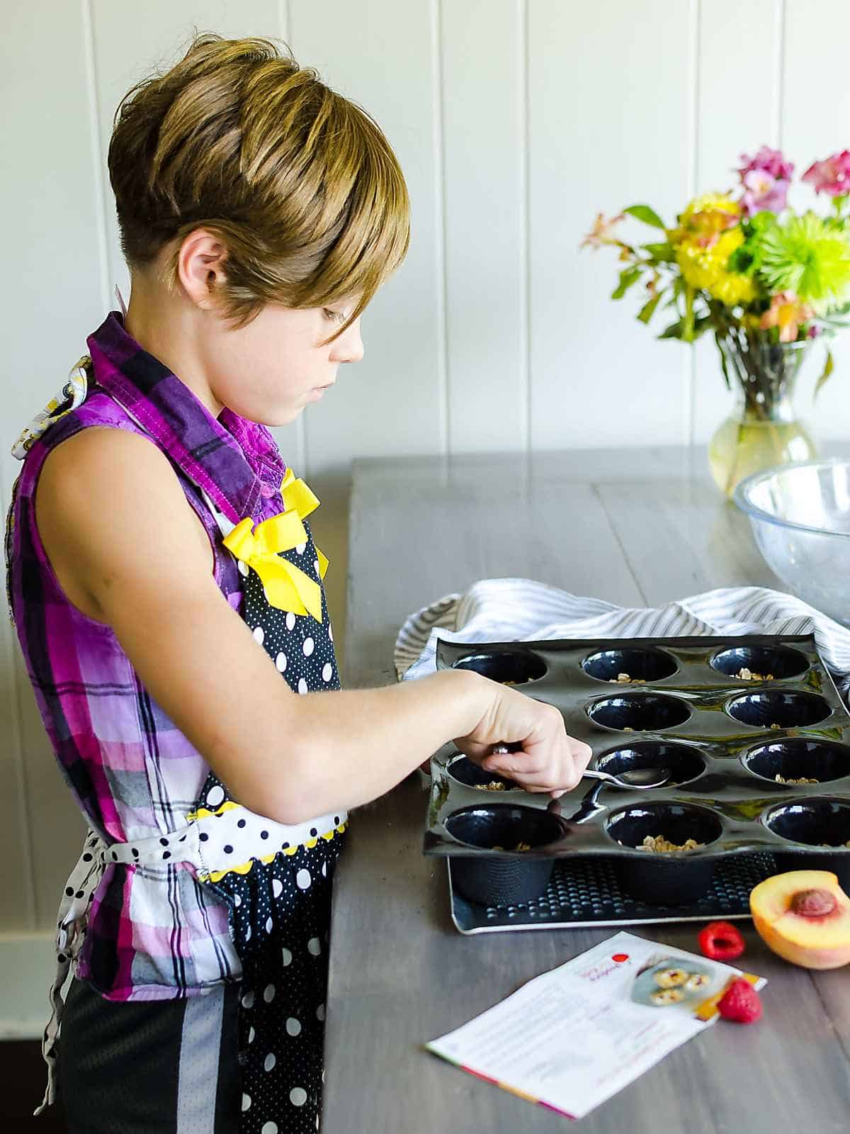 young girl pressing granola mixture into a black muffin tray