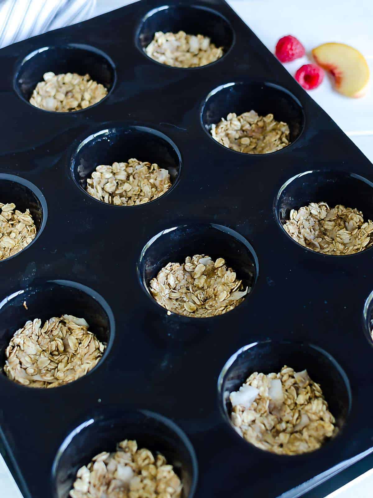 black muffin tray filled with homemade granola pressed into each well to form a mini cup