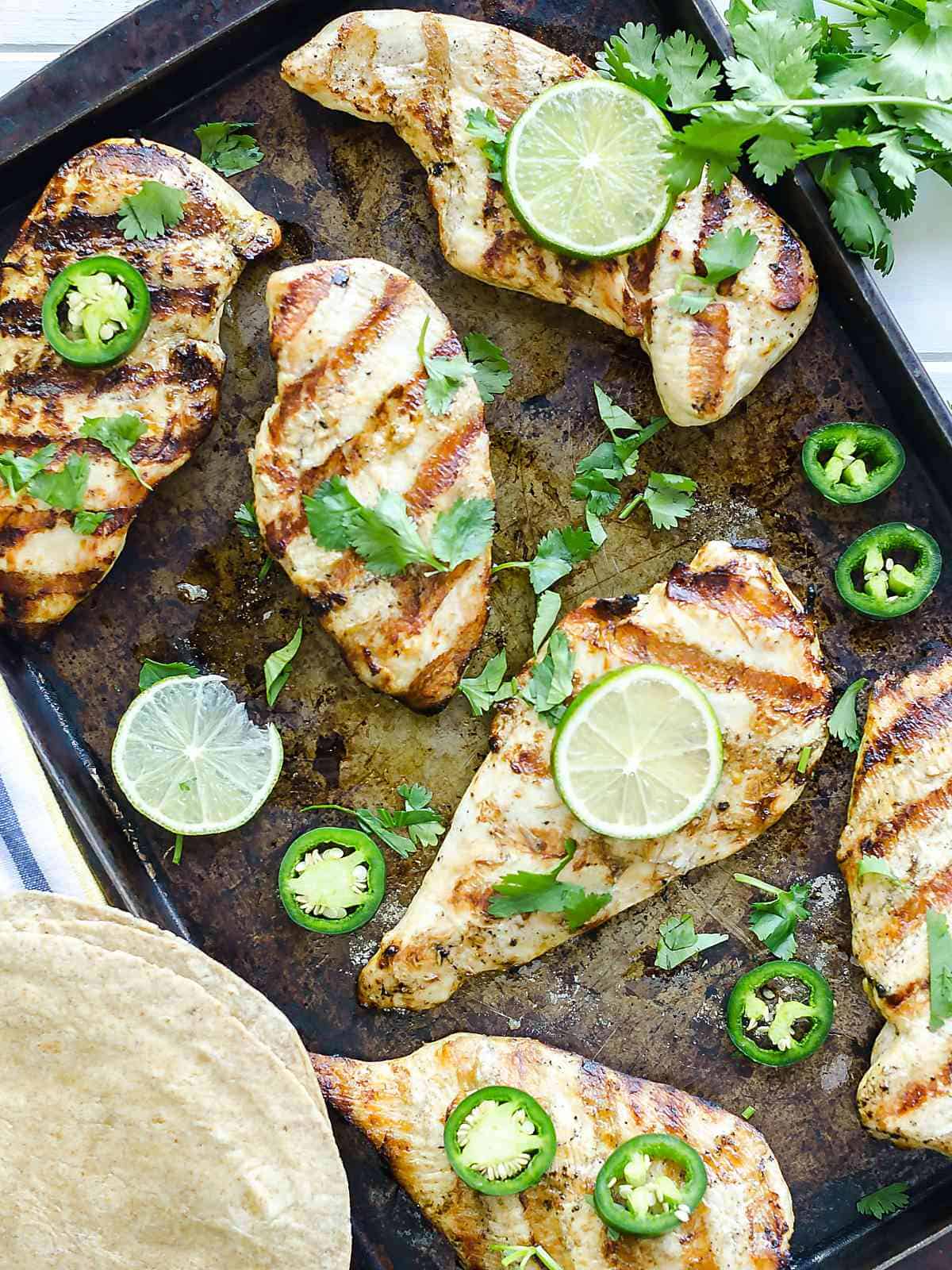 grilled garlic lime chicken breasts garnished with jalapeno , lime slices, and cilantro