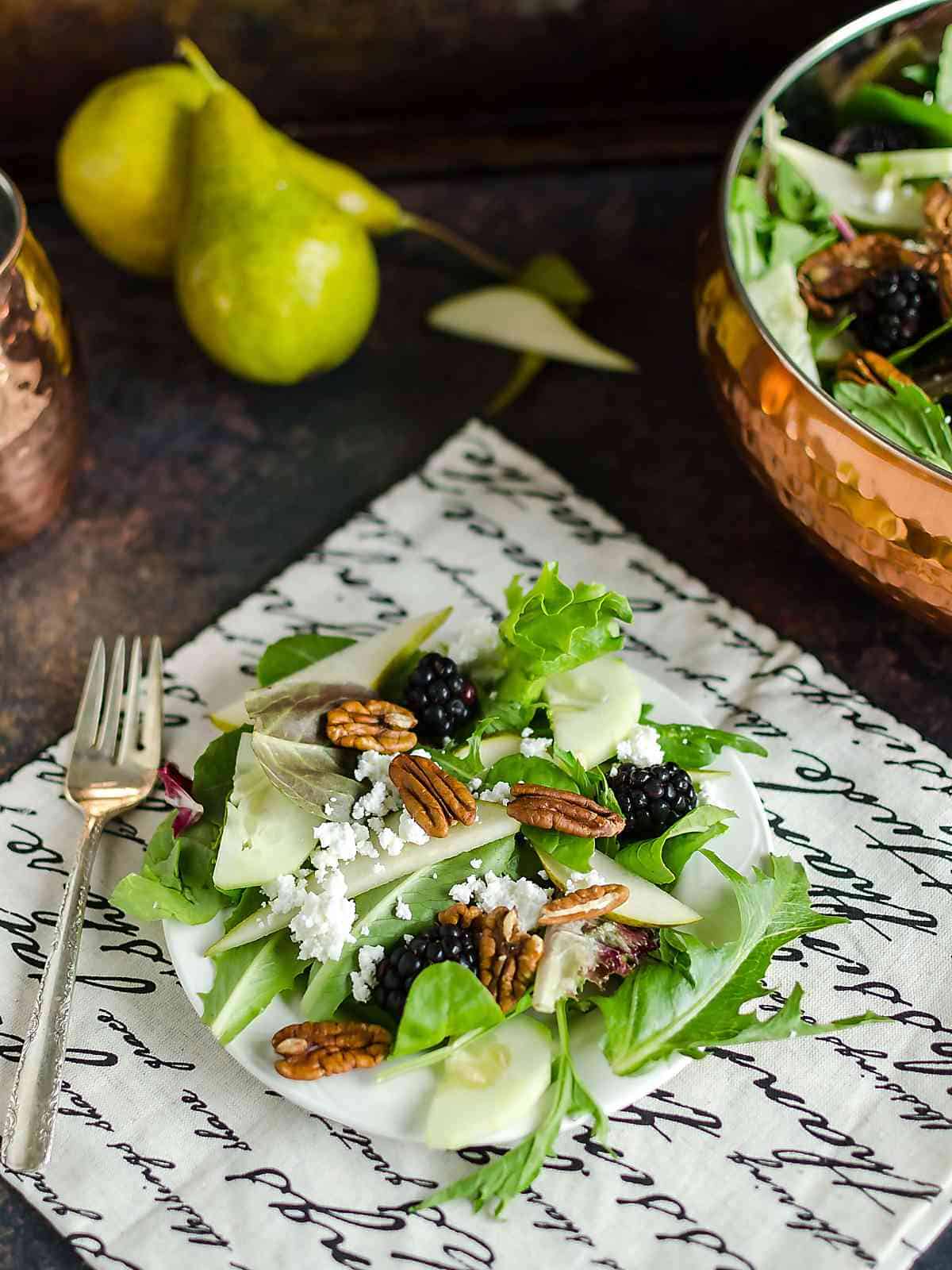 Mixed Greens Salad Recipe ~ a plate full of mixed green salad recipe that contains field greens, fresh pear slices, black berries, crumbled white cheese and pecan halves, bowl of salad in the background and 2 full pears