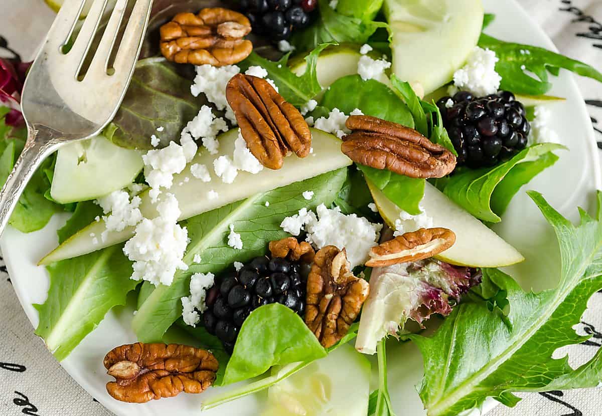 mixed greens, pear slices, blackberries, pecans and crumbled cheese with a fork resting on top