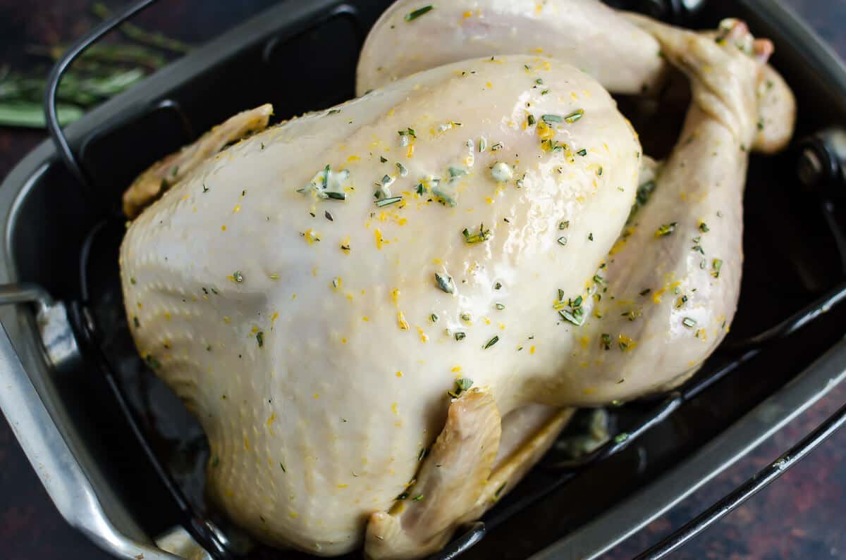 partially cooked whole turkey in a roasting pan with herbed butter gradually melting in to the skin.