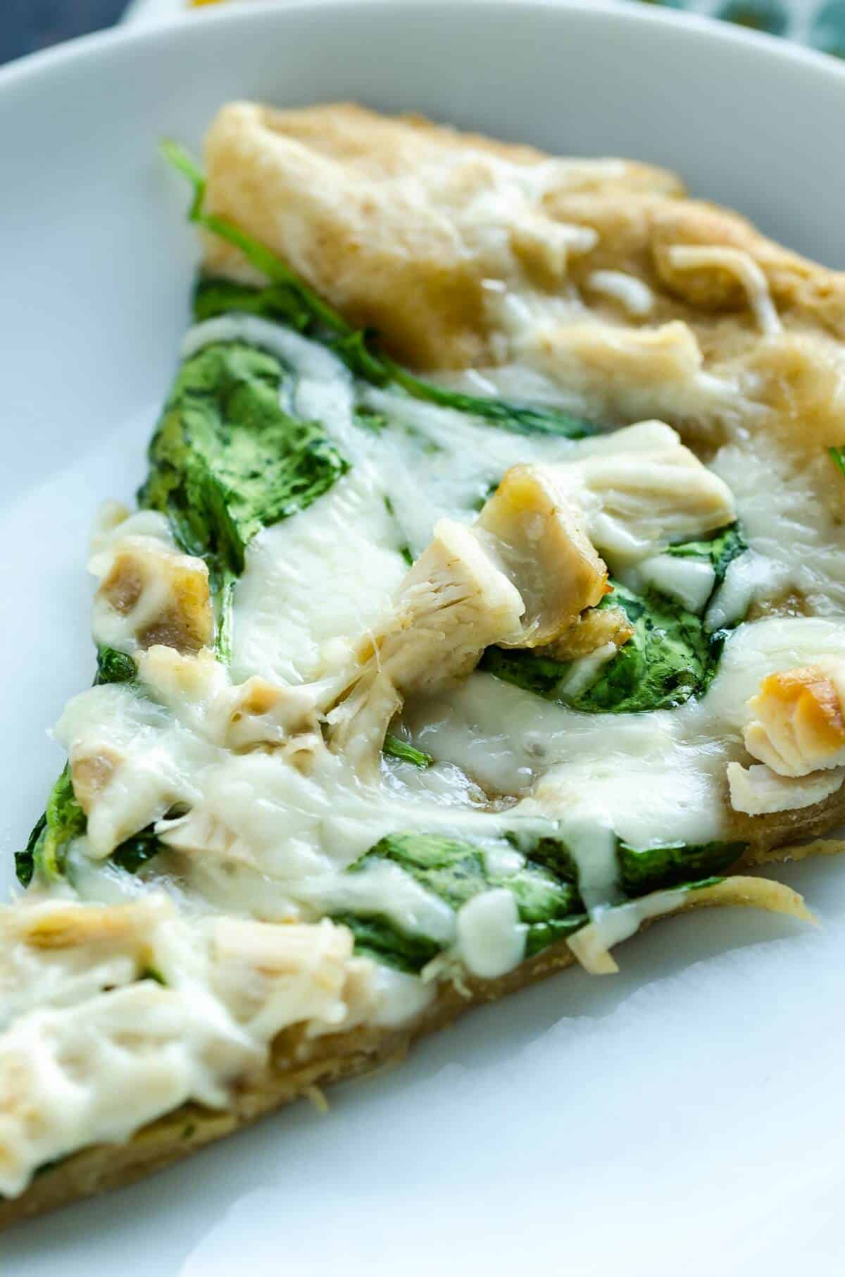slice of hot homemade white pizza, melty cheese, chunks of chicken and spinach leaves