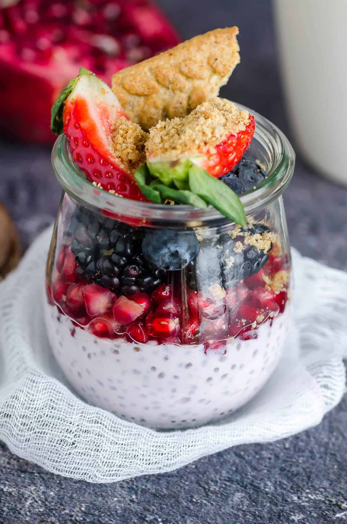 glass jar layered with chia seed pudding, pomegranate arils, blackberries, blueberries, strawberries, and crumbled belVita breakfast biscuit
