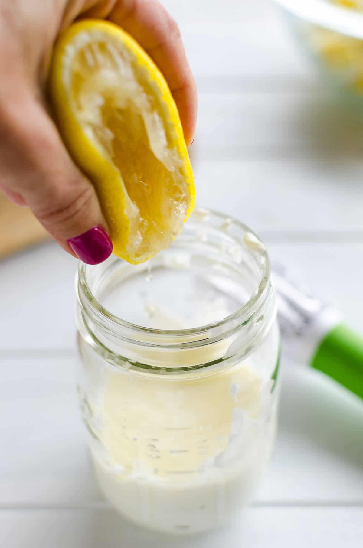 fresh lemon being squeezed into a mason jar of yogurt
