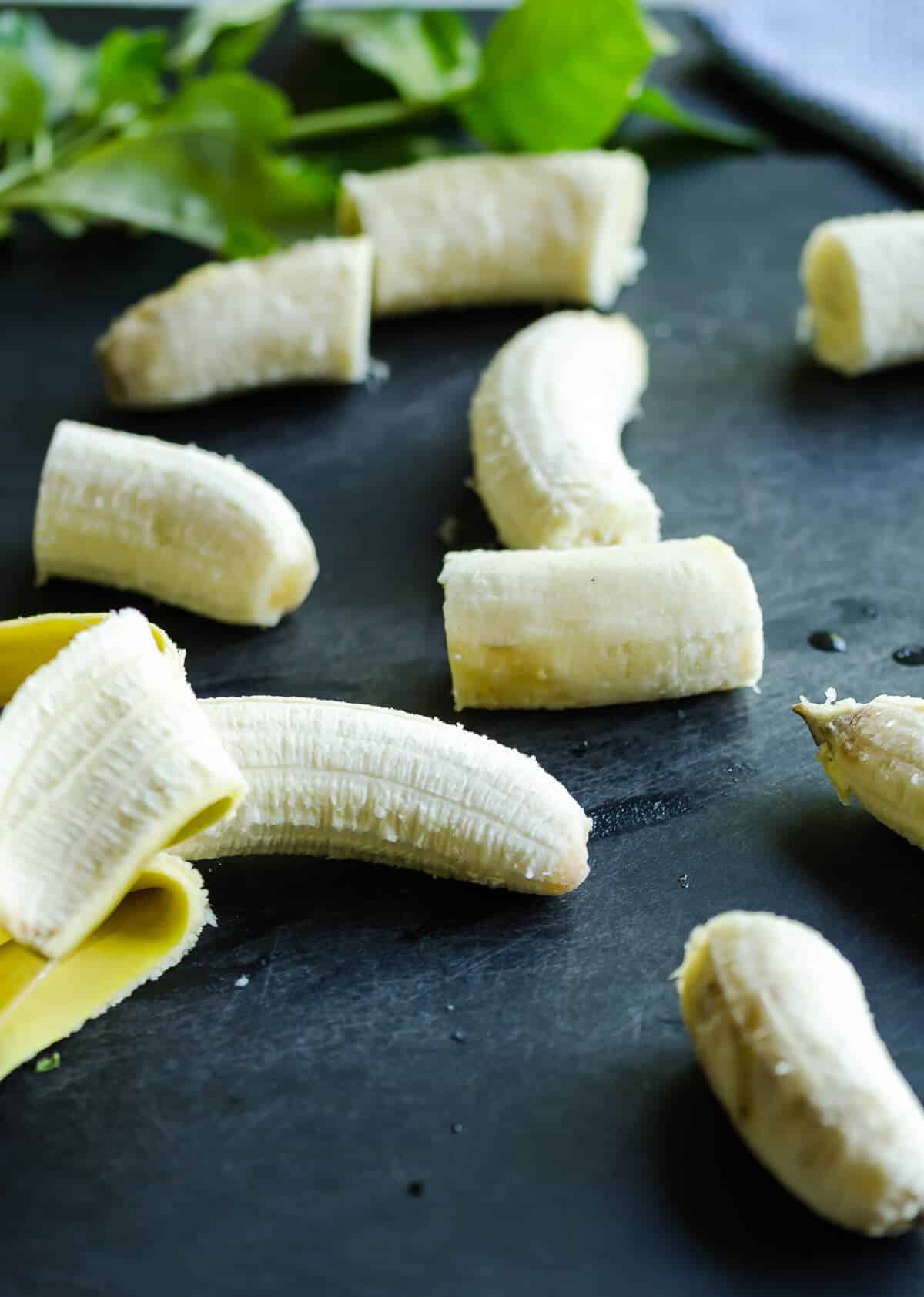 peeled bananas on a cutting board being sliced into thirds