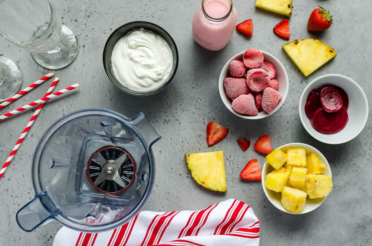 ingredients for strawberry pineapple smoothie: yogurt, strawberry milk, frozen strawberries, frozen pineapple, beet juice, blender
