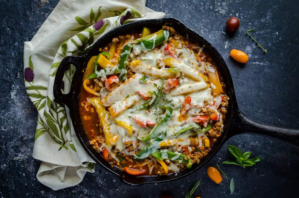 overhead view of a cast iron skillet filled with unstuffed peppers made with ground turkey, colored peppers and covered in melted cheese.