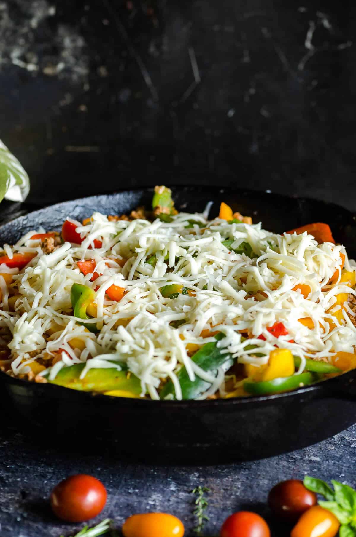 cast iron skillet filled with low carb unstuffed peppers made with ground turkey and cauli rice and sprinkled with cheese ready to go in the oven.