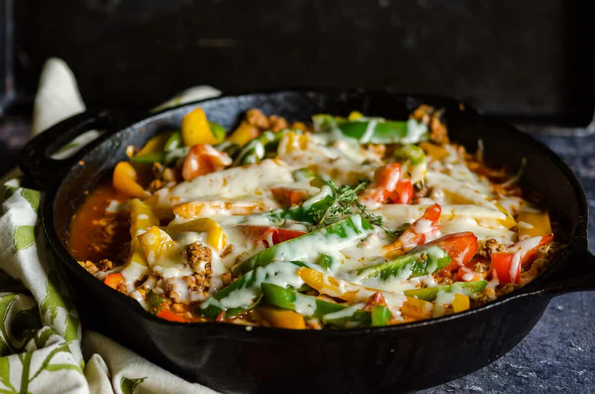 cast iron skillet filled with cooked ground turkey in an Italian sauce with sliced of colored bell peppers and melted cheese.