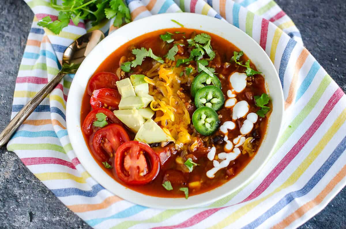 bowl of turkey taco soup garnished with sliced cherry tomatoes, avocados, cheese, jalapeños, and yogurt