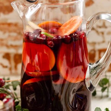 kirkas lasinen kannu täynnä alkoholitonta punaista Sangria Mocktailia, tuoretta greippiä, appelsiineja, kakia, and cranberries