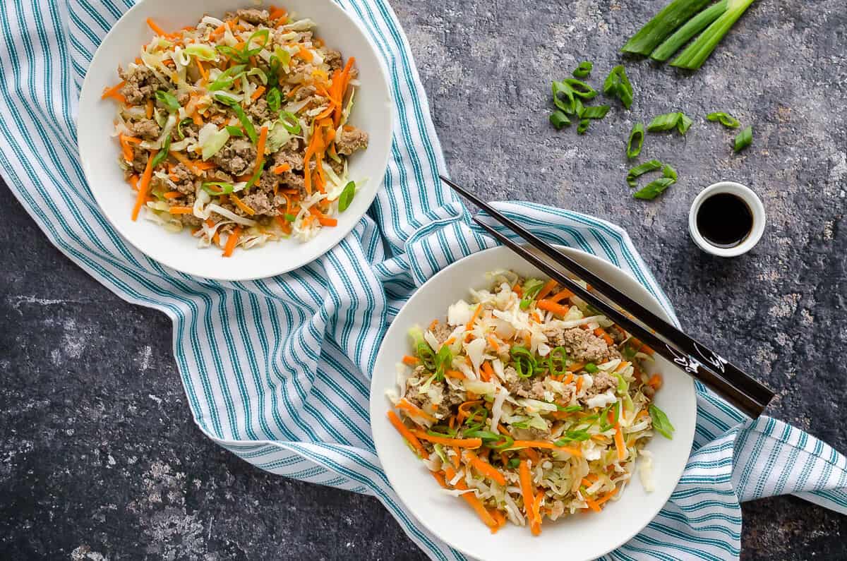 2 white bowls filled with cooked ground turkey, cole slaw and seasonings to form egg roll in a bowl (a deconstructed egg roll without the wrapper).