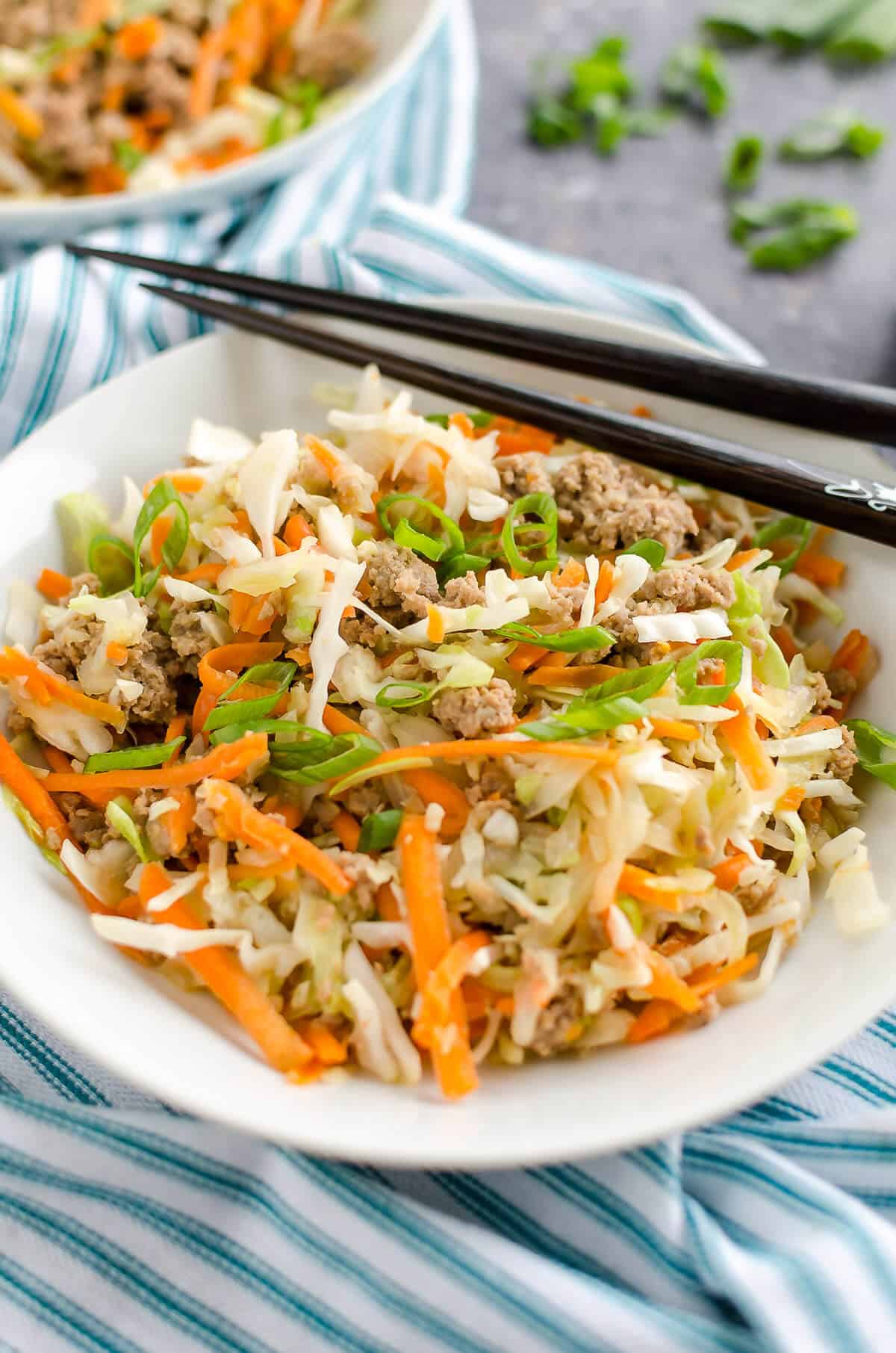 white bowl filled with cooked ground turkey, shredded cabbage, shredded carrots and seasonings to create a deconstructed egg roll. chopsticks laying over top of the bowl.